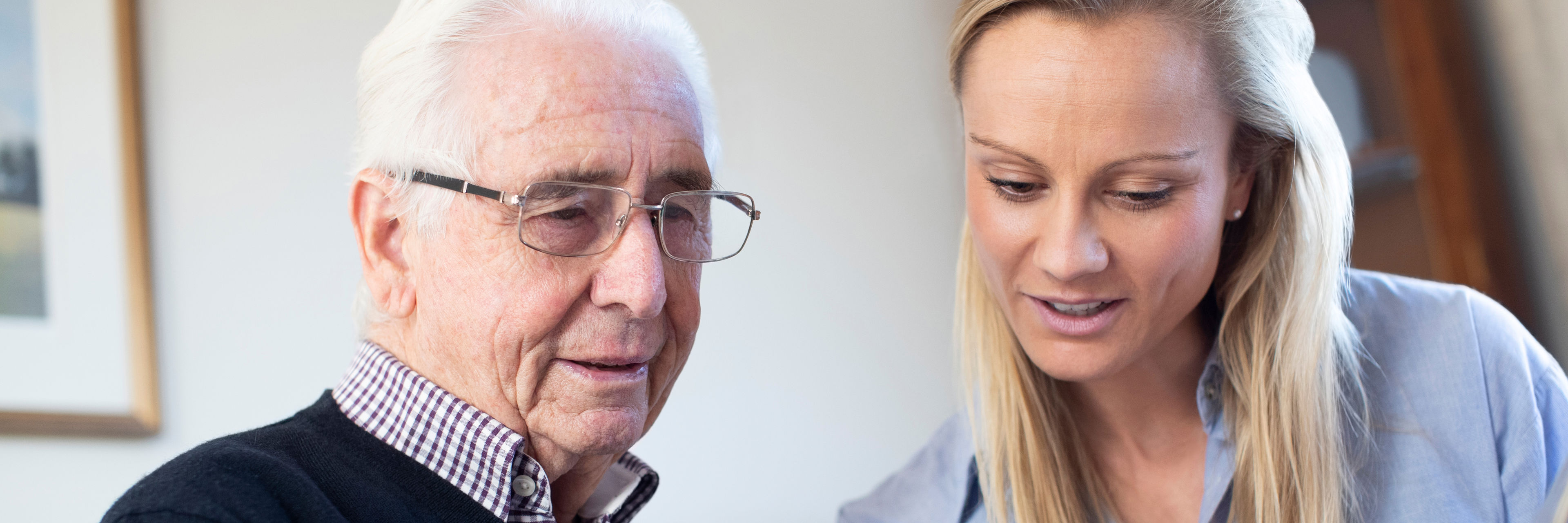 Ældre mand kigger på billeder med en lyshåret kvinde. Kvinden peger på et billede. Manden ser ud til at genkende det.
